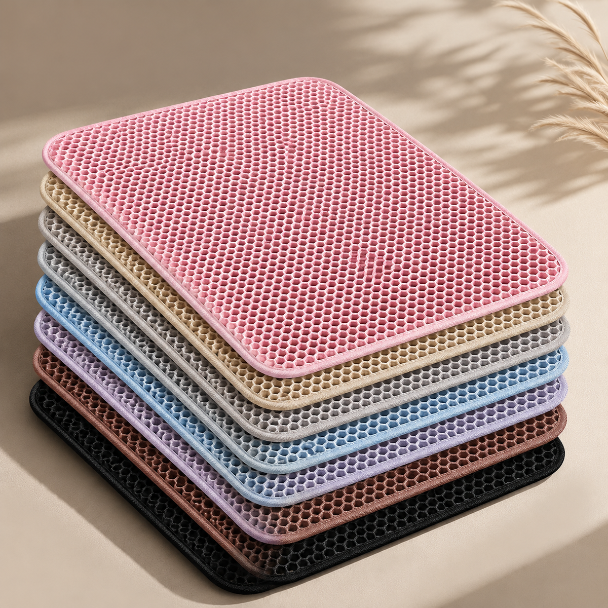 A stack of rectangular honeycomb-textured cooling mats in multiple pastel and neutral colors, including pink, beige, gray, blue, mauve, brown, and black, arranged on a warm beige surface with soft shadows.