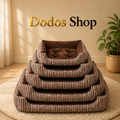 Five nested rectangular pet beds with striped brown, beige, and teal fabric and a tufted brown cushion inside each bed, stacked on a cream rug in a warm room. The words 'Dodos Shop' appear above the beds.